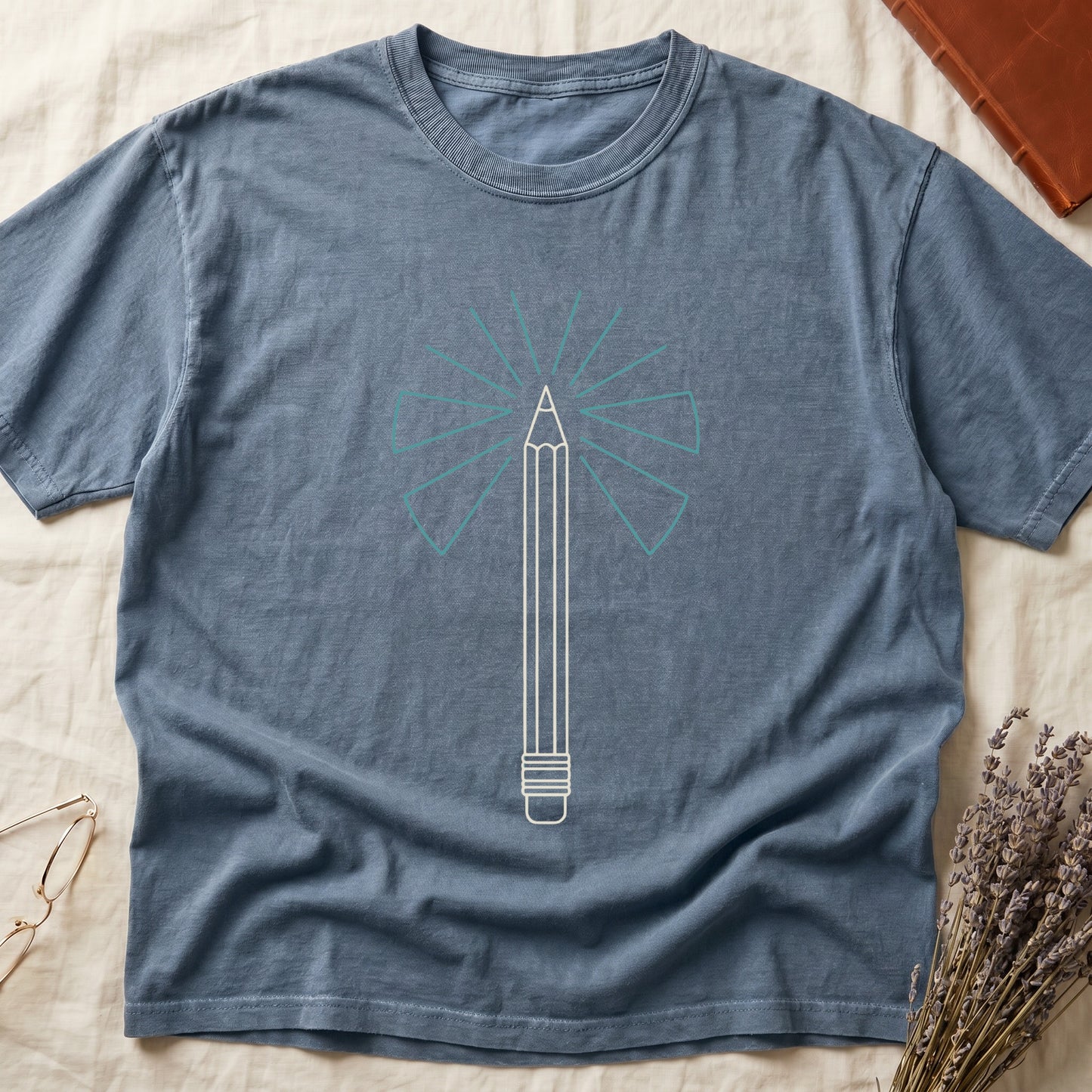 Blue Jean tee with single vertical graphite pencil in cream linework, fan of teal and grey rays radiating behind.