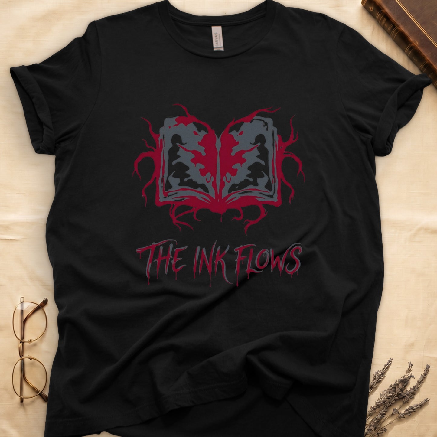 Black tee with open book bleeding red ink into a gray face on green ground, "THE INK FLOWS" in dripping serif.