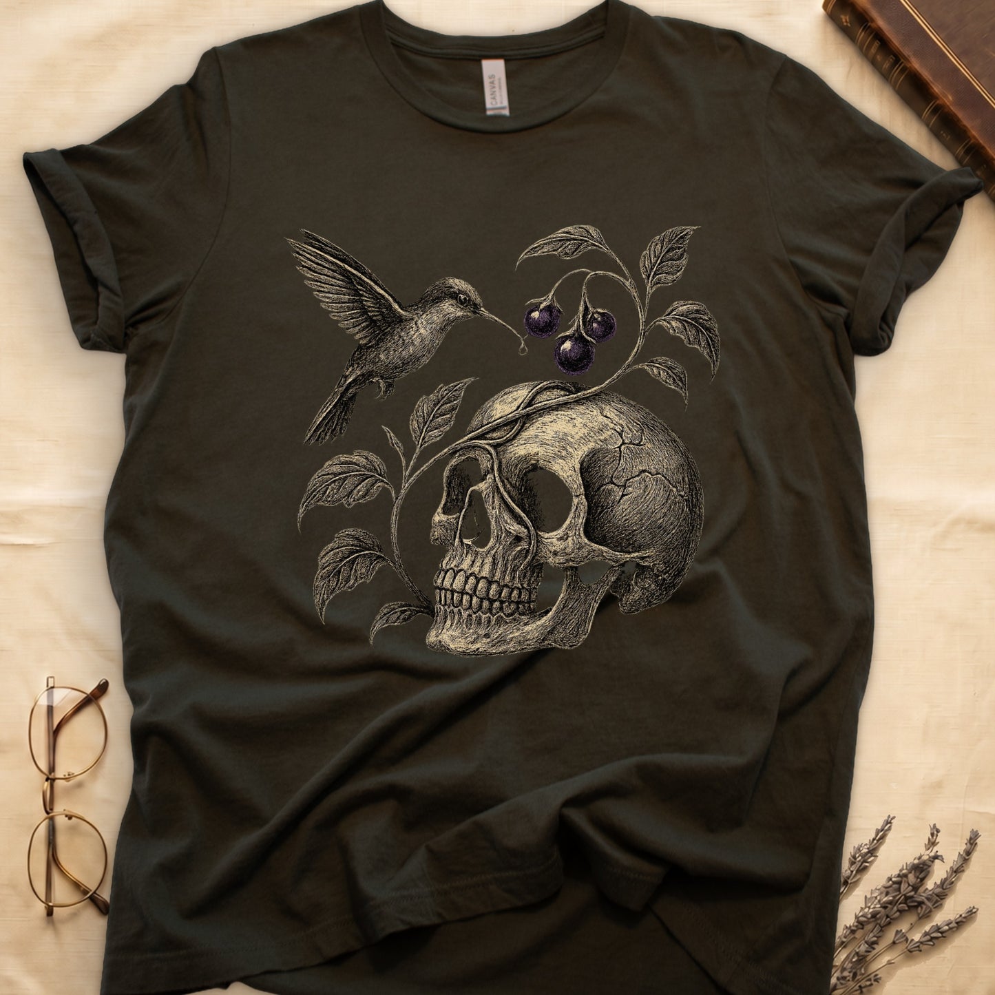 Military Green tee with sepia engraved skull, nightshade vine and dark-purple berries wrapping around, hummingbird at upper left.