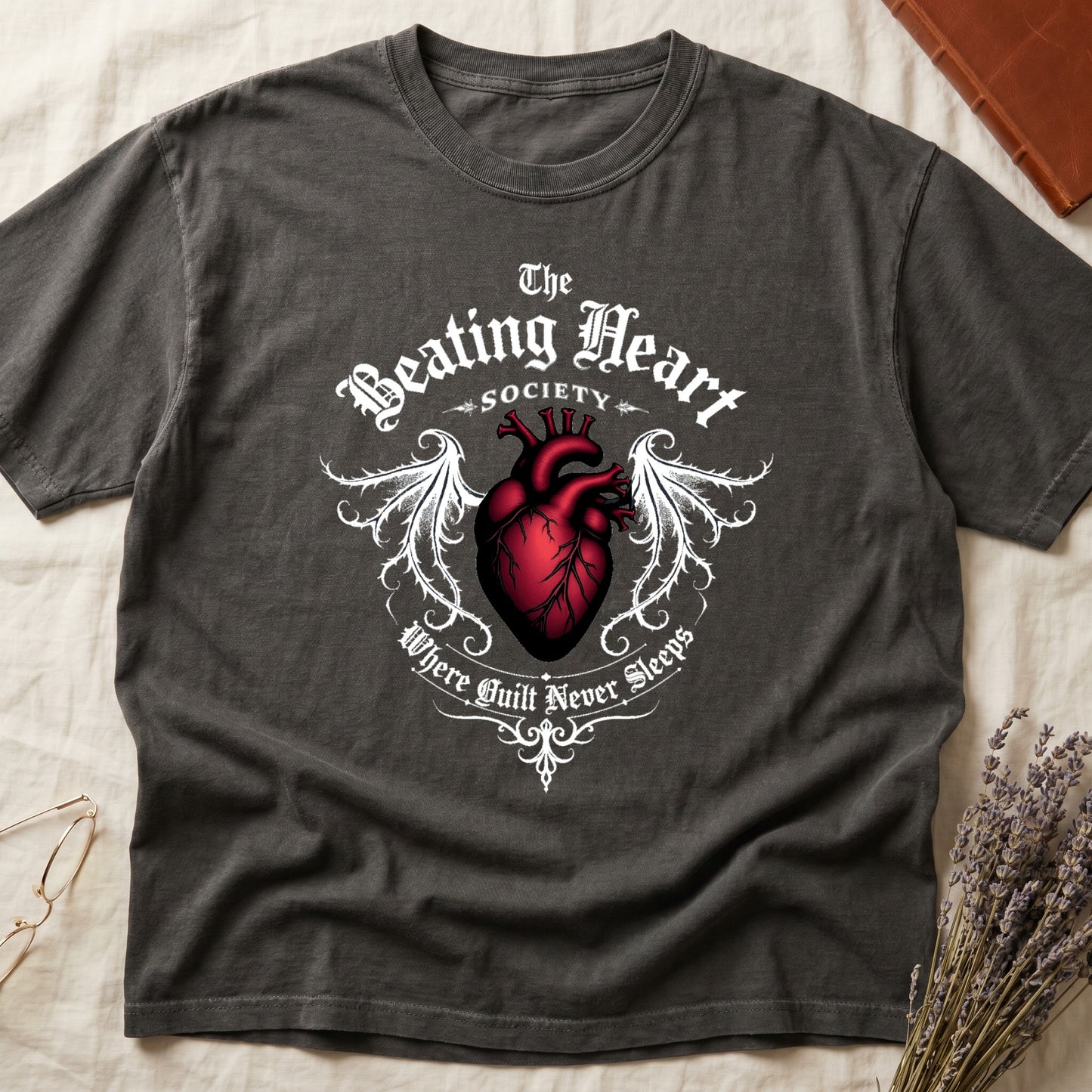 Pepper tee with anatomical red heart, gothic wings, "The Beating Heart SOCIETY," "Where Guilt Never Sleeps" below.