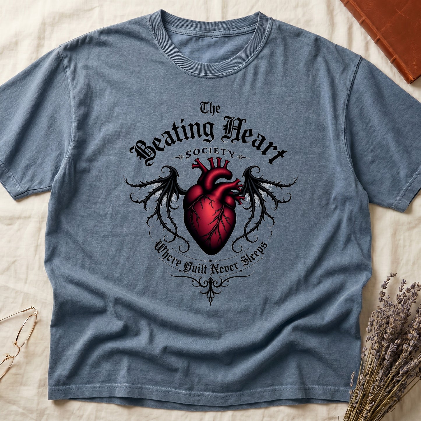 Blue Jean tee with anatomical red heart, gothic wings, "The Beating Heart SOCIETY," "Where Guilt Never Sleeps" below.