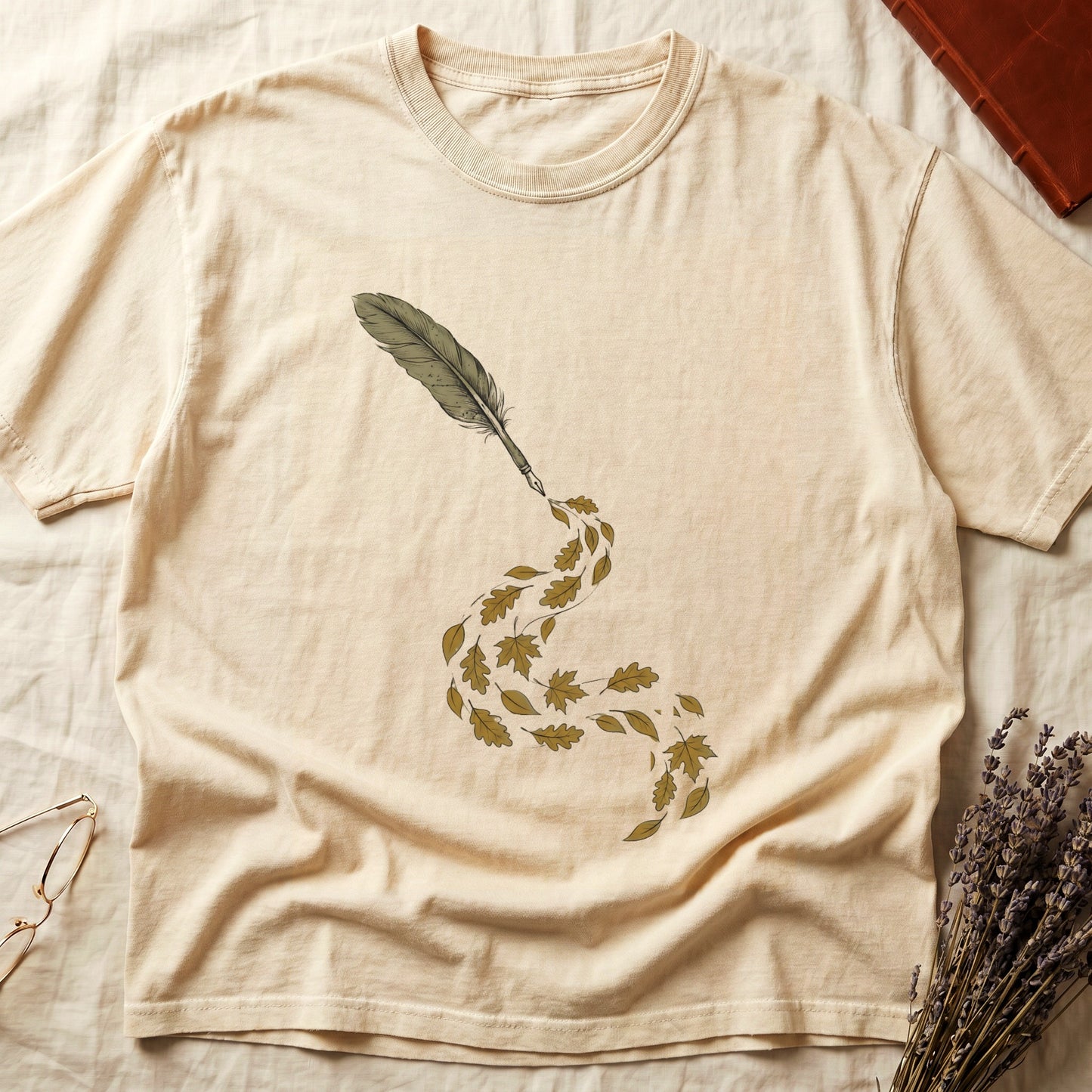 Ivory tee with antique quill pen in cream linework, oak and maple leaves cascading from the nib in gold and green.