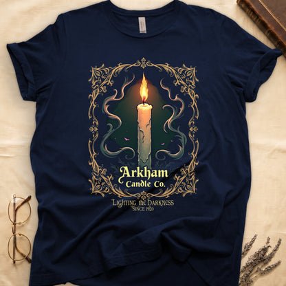 Navy tee with lit candle, smoke, ornate gold filigree border, "Arkham Candle Co.," "Lighting the Darkness Since 1920."