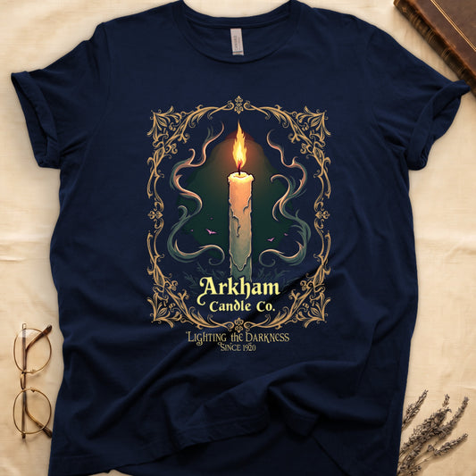 Navy tee with lit candle, smoke, ornate gold filigree border, "Arkham Candle Co.," "Lighting the Darkness Since 1920."