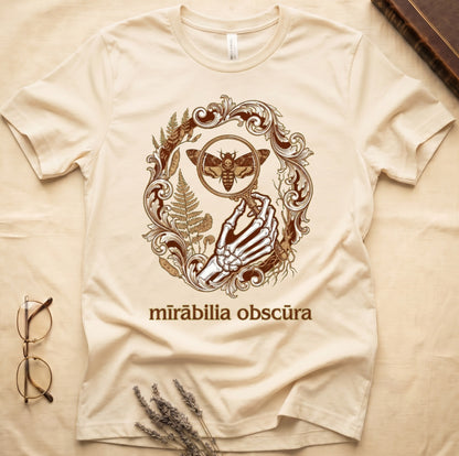 Natural tee with skeletal hand, magnifying glass, death's-head moth, ferns on green, "mīrābilia obscūra" in Latin italic.