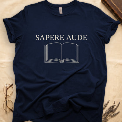 Navy tee with "SAPERE AUDE" in serif capitals above a minimalist open book in cream linework.