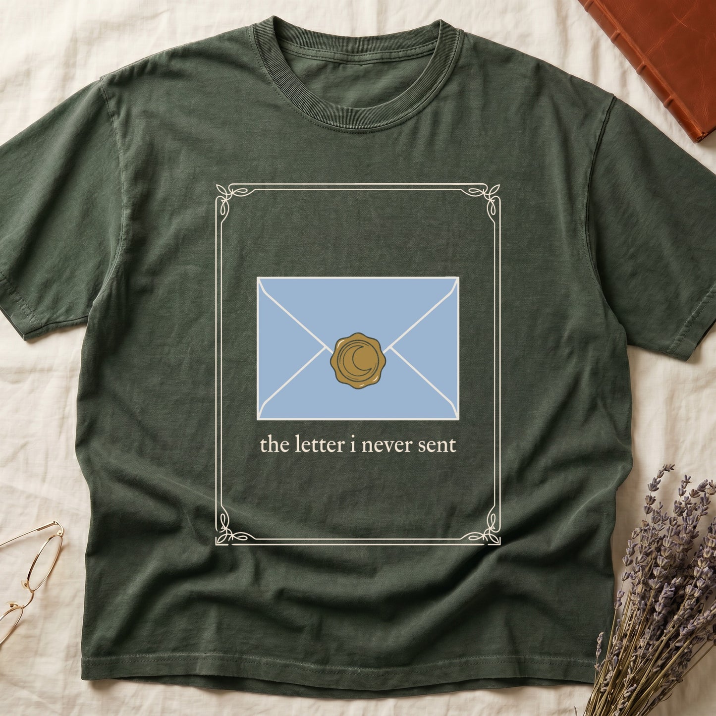 Green tee with pale blue envelope sealed with gold crescent moon wax seal, "the letter i never sent" cream serif below.
