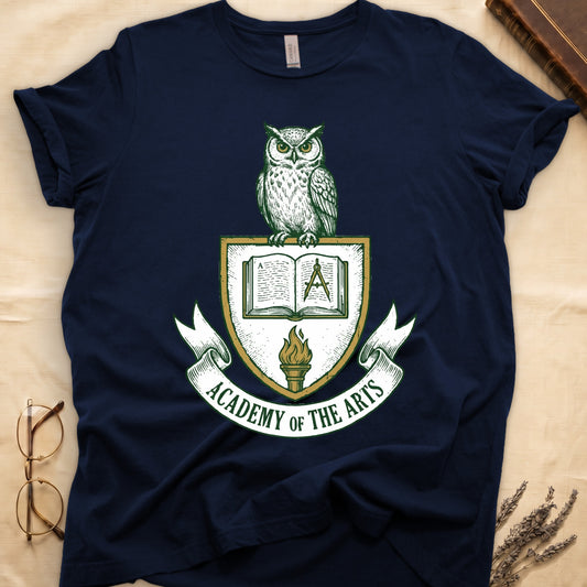 Navy tee with heraldic shield crest, owl perched on top, open book and dividers center, "ACADEMY OF THE ARTS" on a banner.