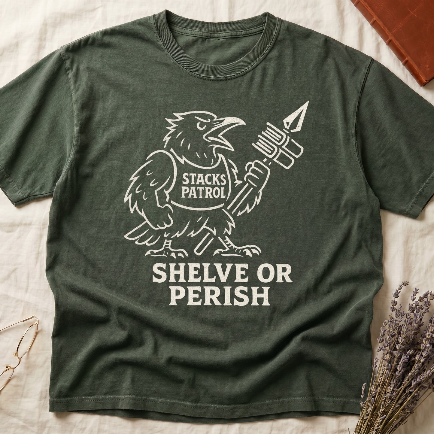 Green tee with vintage raven mascot, "STACKS PATROL" sash, feather pen aloft, "SHELVE OR PERISH" bold serif below.