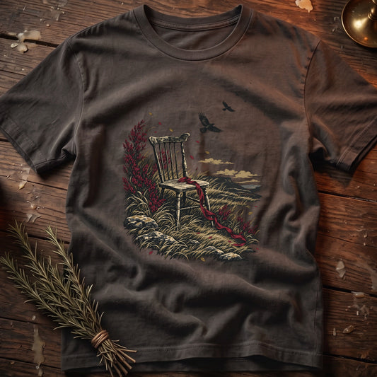 T-shirt with vintage chair, red ribbon, and raven graphic on grassy landscape.