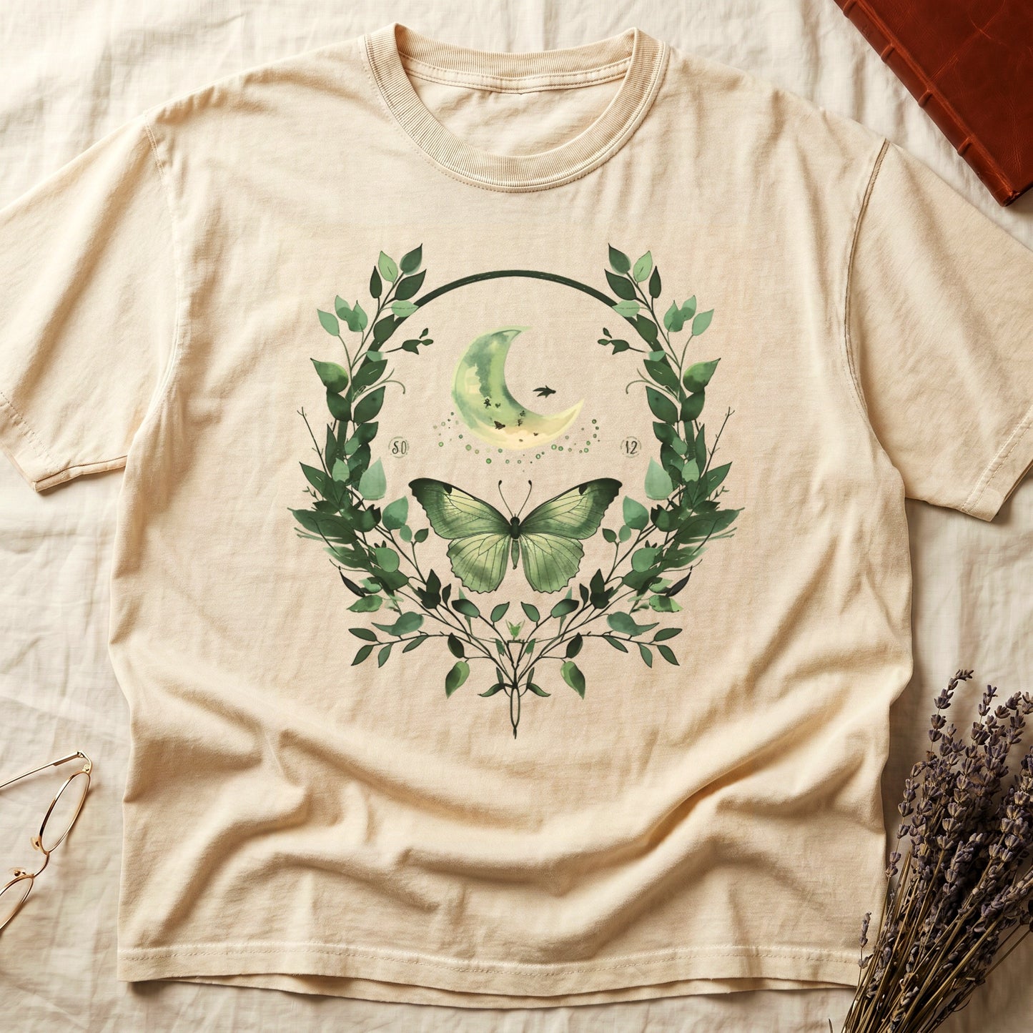 T-shirt with green butterfly, crescent moon and foliage wreath graphic.