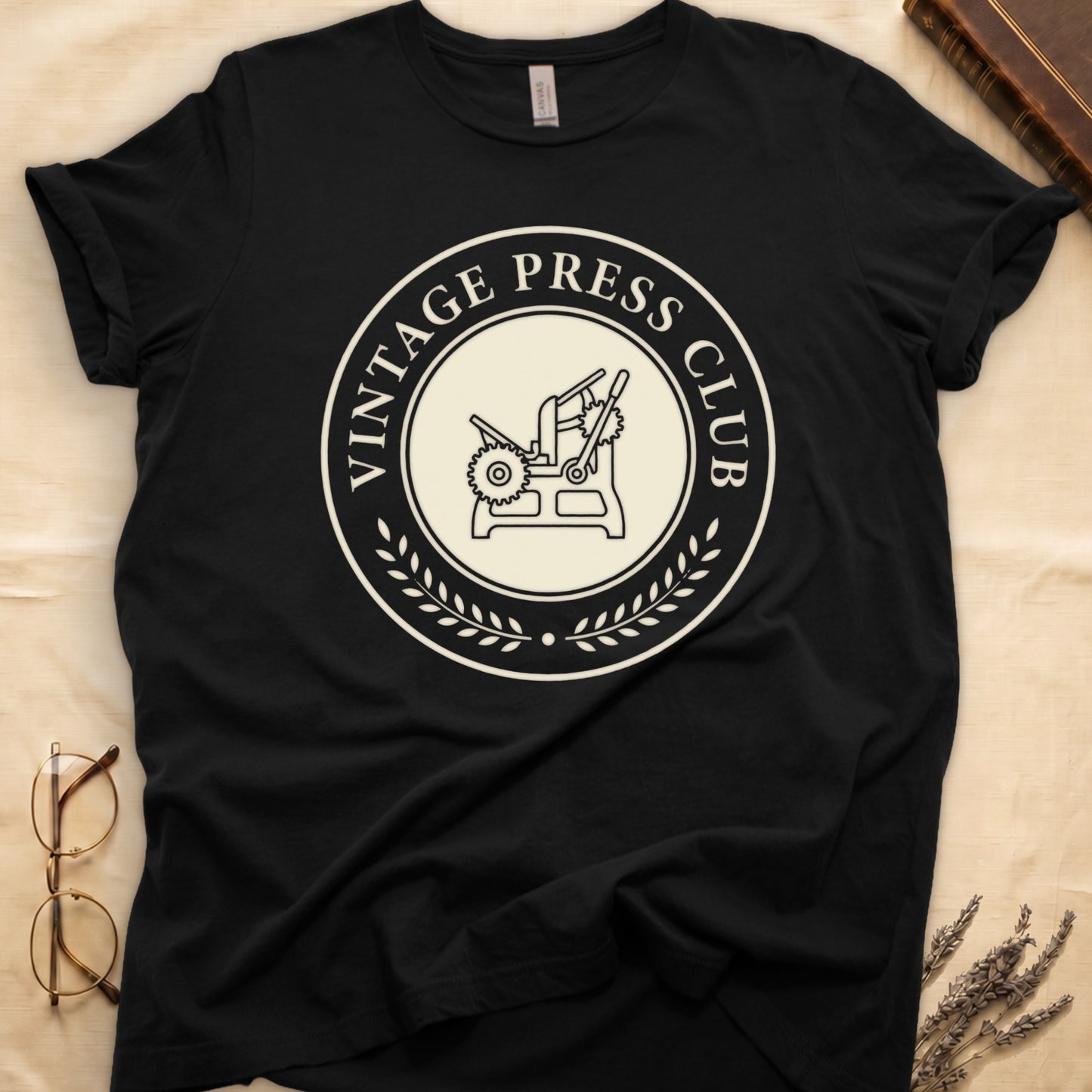 Black tee with circular letterpress badge, "VINTAGE PRESS CLUB" in serif capitals, antique printing press in cream linework.