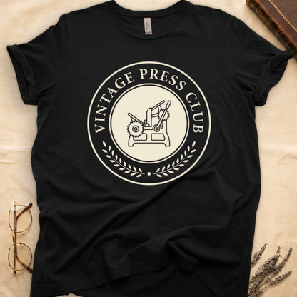 Black tee with circular letterpress badge, "VINTAGE PRESS CLUB" in serif capitals, antique printing press in cream linework.