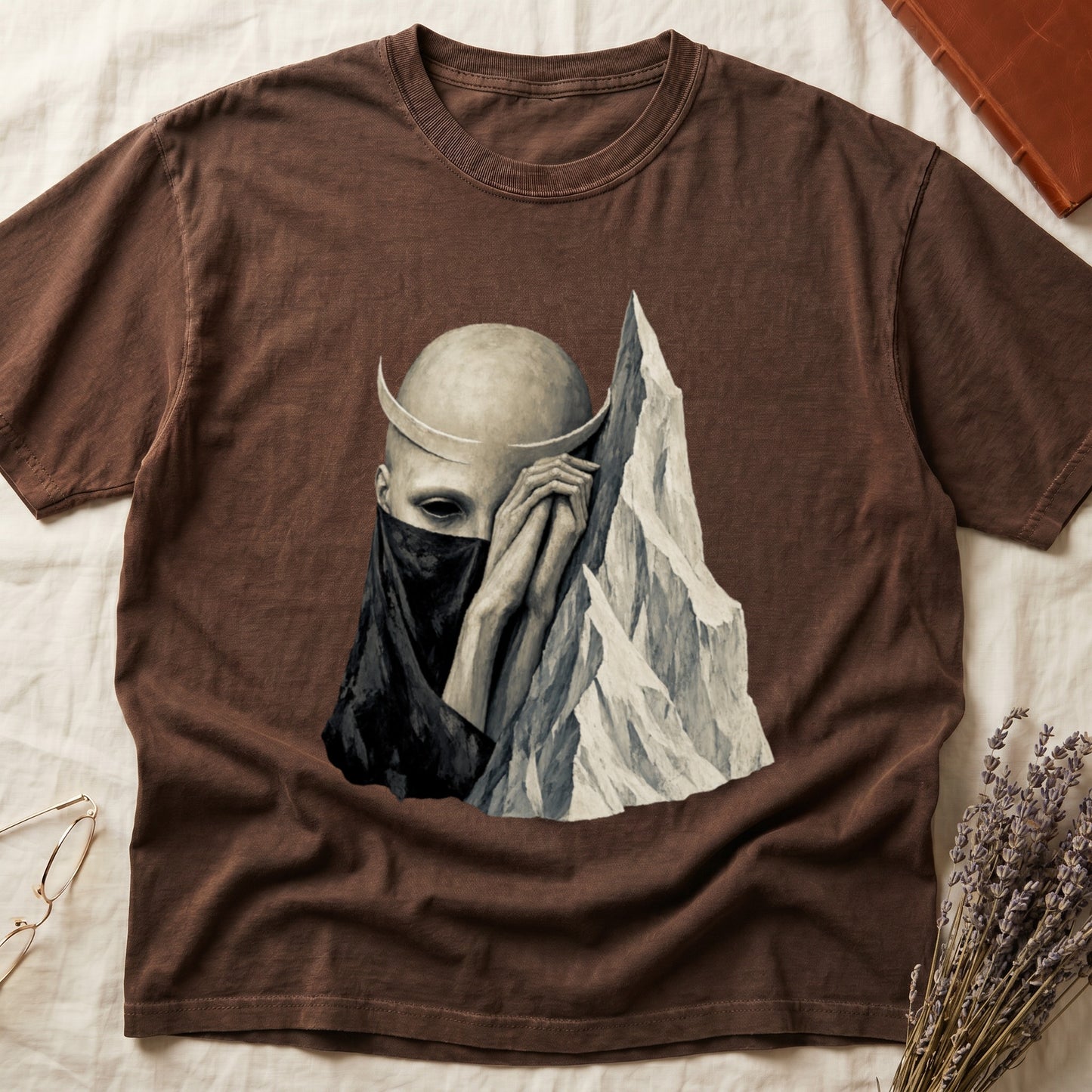 Brown t-shirt with illustration of a veiled figure with crescent horns and mountains.