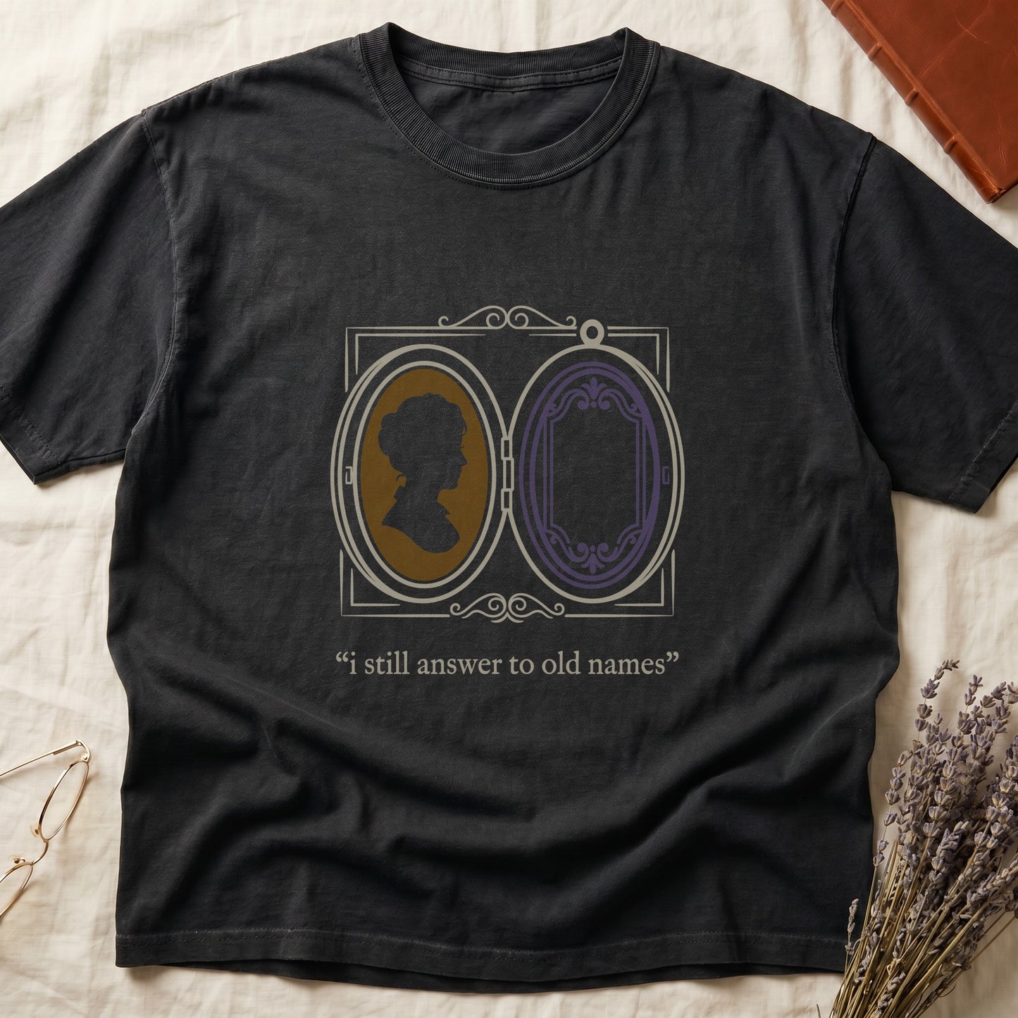 Black tee with Victorian double-locket, silhouette portrait in gold frame, "i still answer to old names" cream serif below.