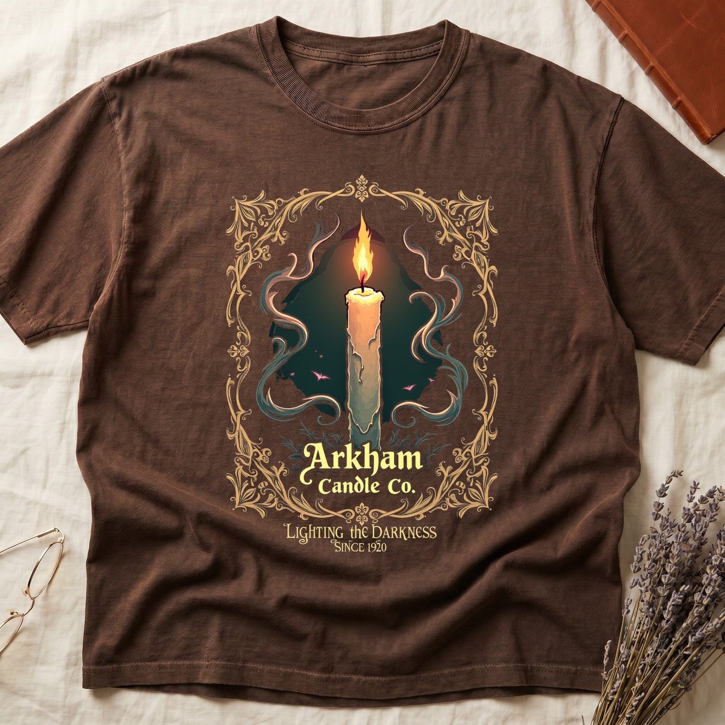 Espresso tee with lit candle, smoke, ornate gold filigree border, "Arkham Candle Co.," "Lighting the Darkness Since 1920."