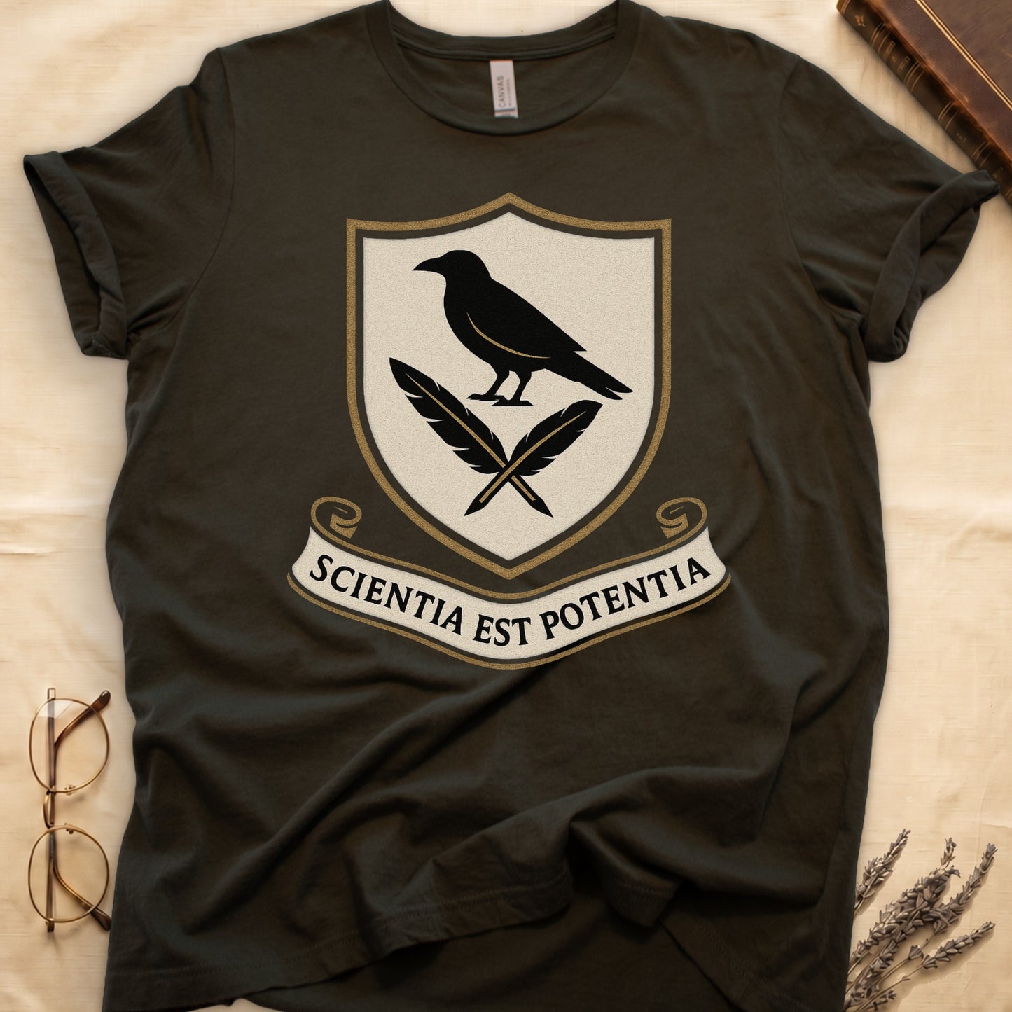 Military Green tee with cream-and-gold heraldic shield, black raven over crossed quills, scroll banner "SCIENTIA EST POTENTIA" below.