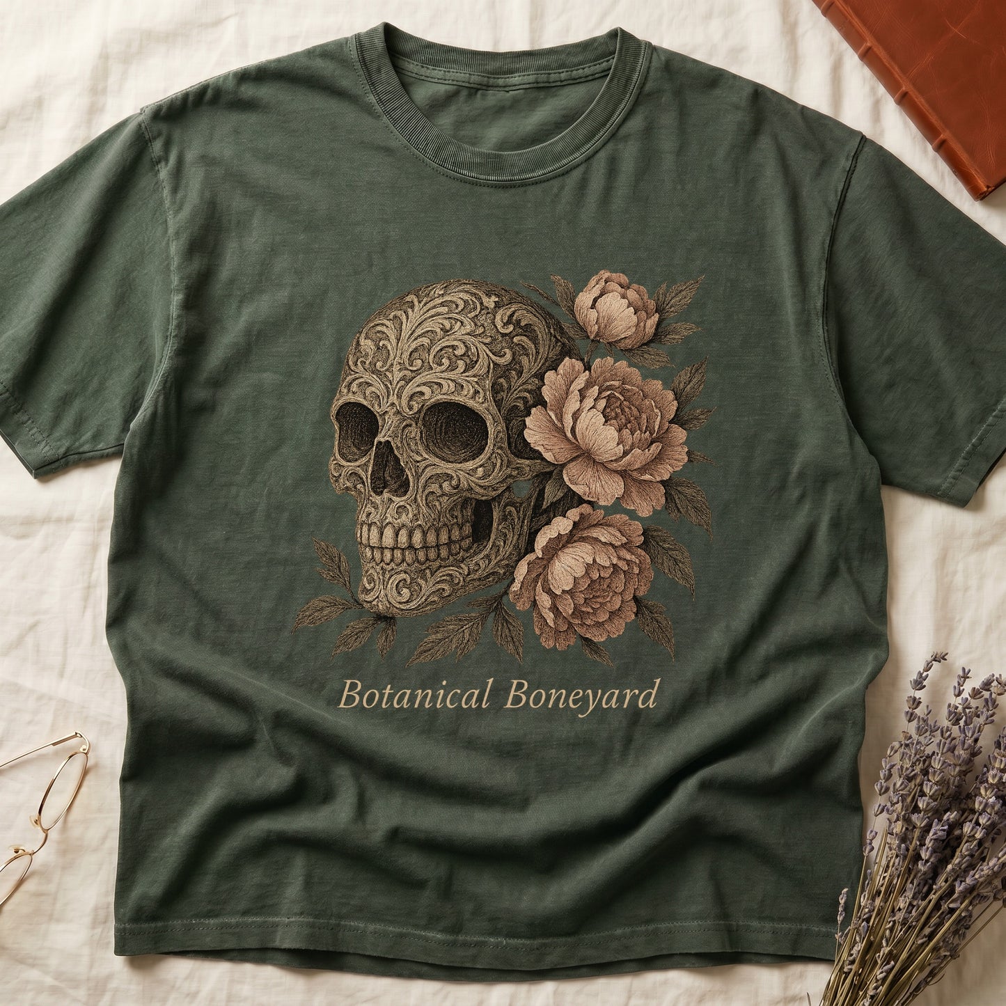 Green tee with filigree-engraved skull on left, peach-cream peonies on right, crossed bones below, "Botanical Boneyard."