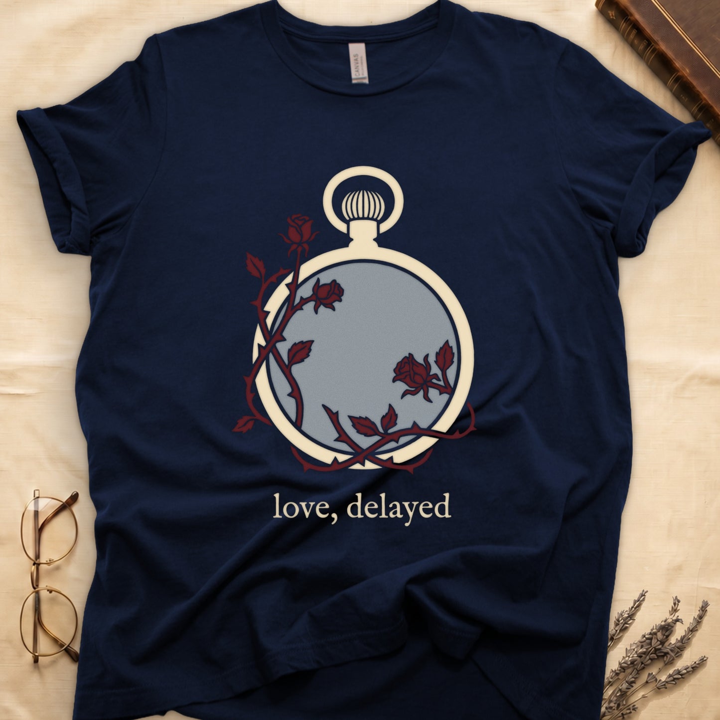Navy tee with vintage cream pocket watch and dark red roses entwined, "love, delayed" in cream serif below.