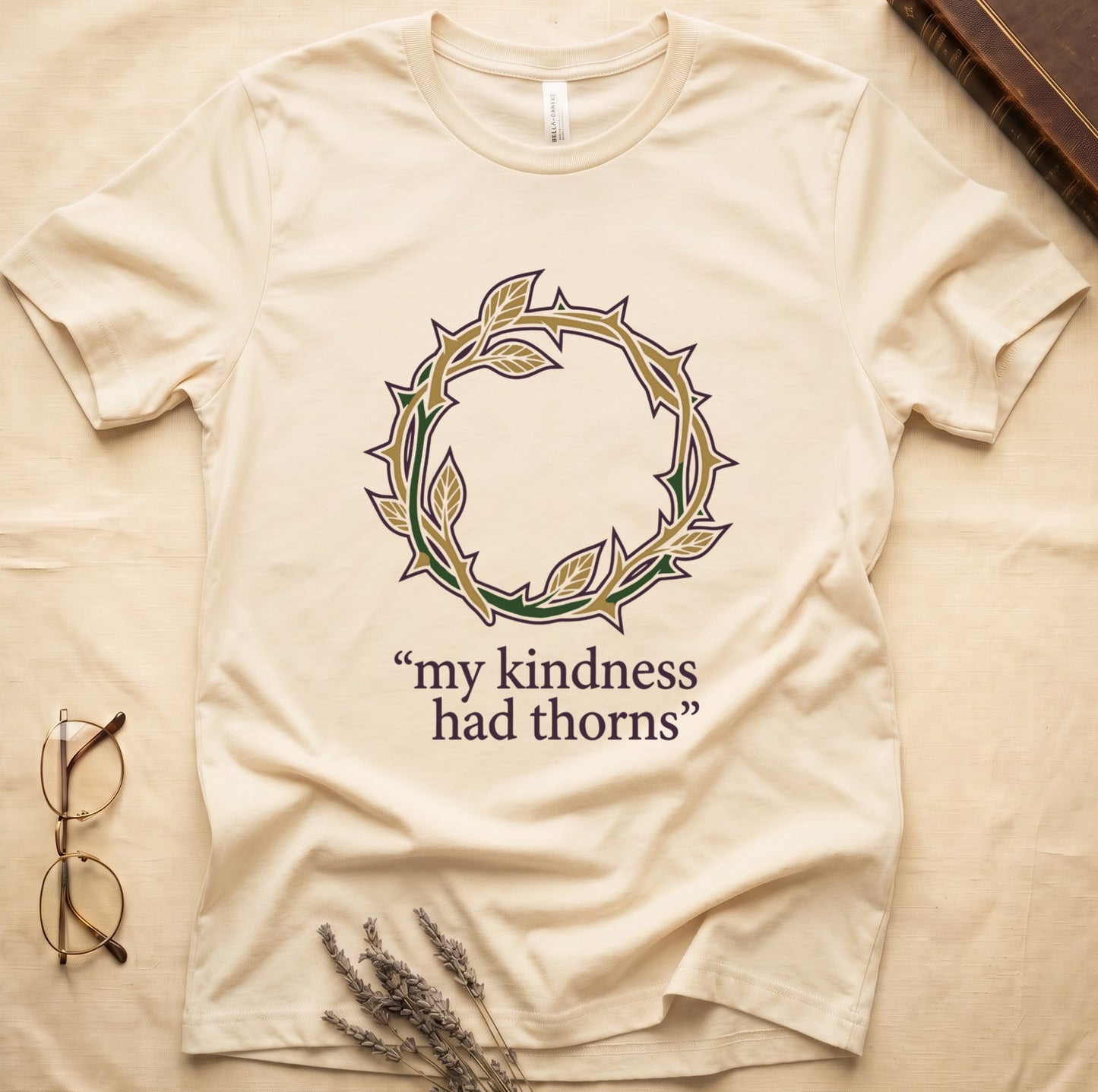 Natural tee with crown of thorns in gold and red with green leaves, "my kindness had thorns" in cream serif.