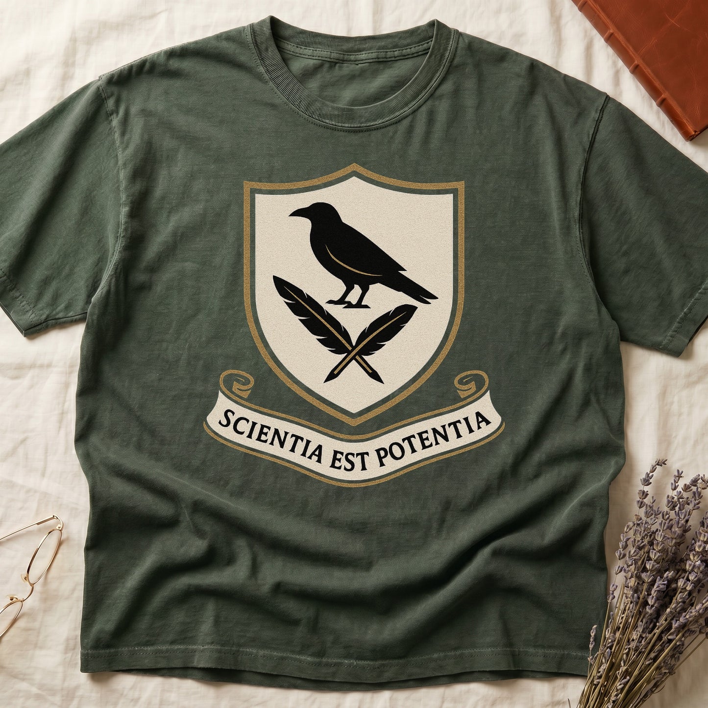 Green tee with cream-and-gold heraldic shield, black raven over crossed quills, scroll banner "SCIENTIA EST POTENTIA" below.