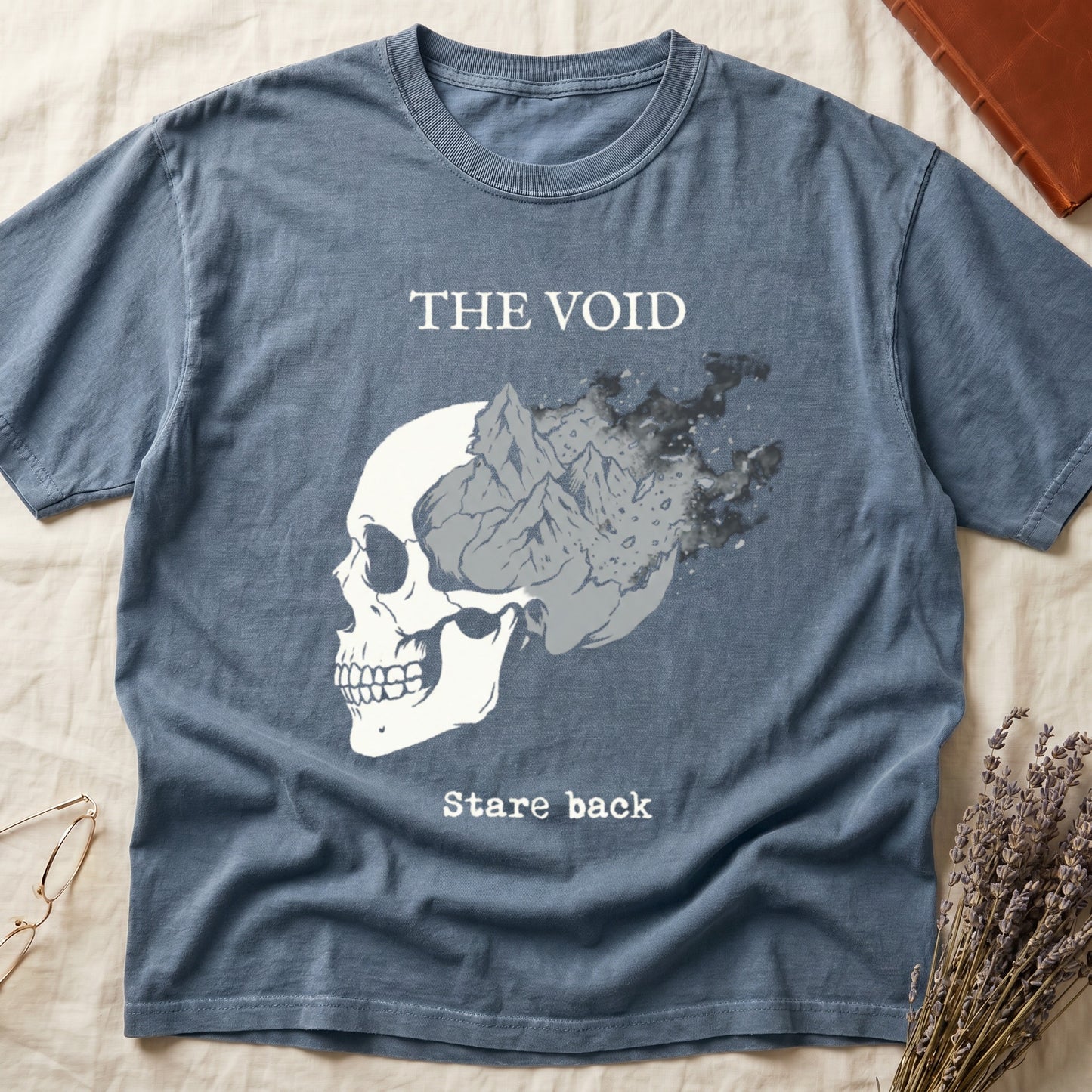 Blue Jean tee with skull eroding into mountain landscape and stardust, "THE VOID" top, "Stare back" typewriter below.