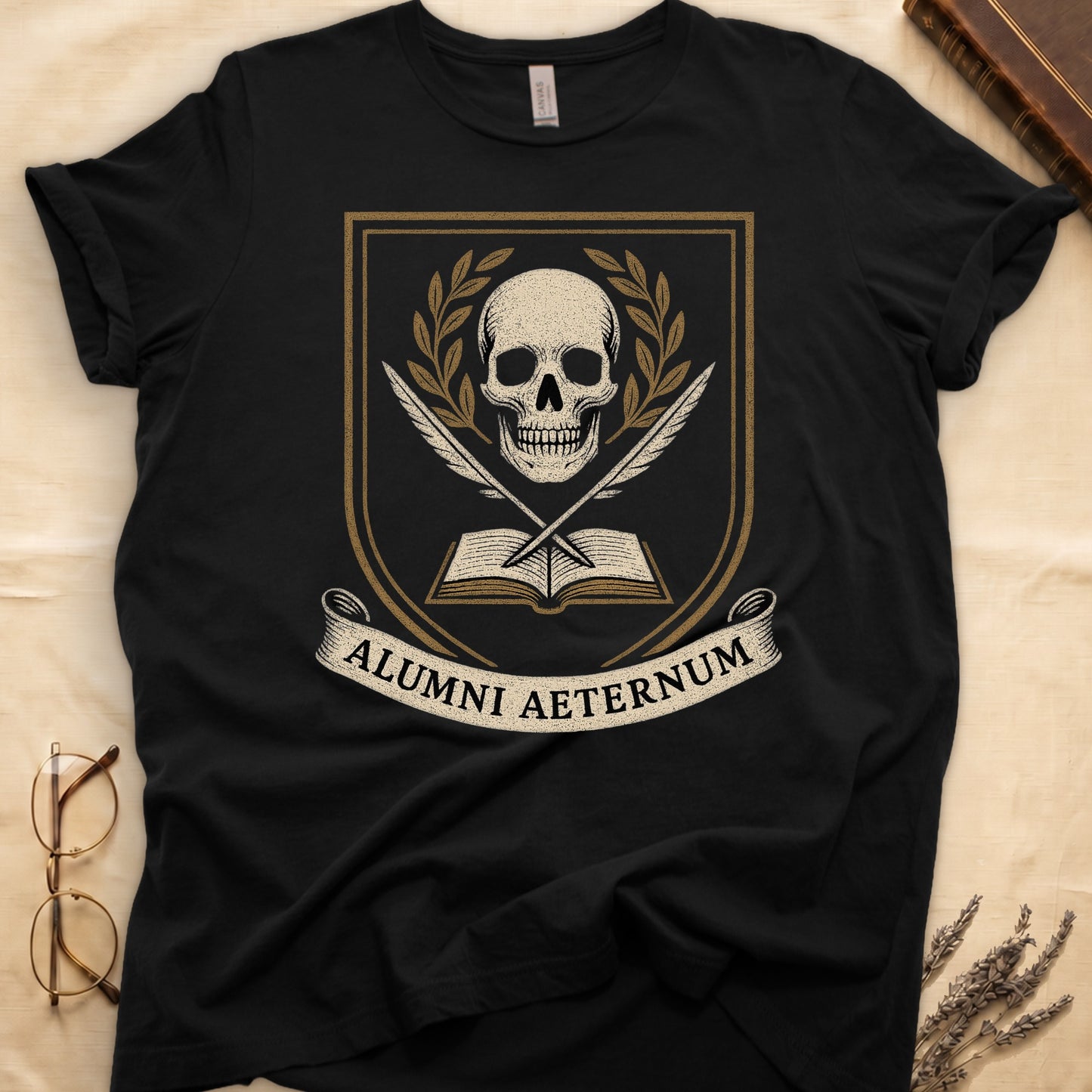 Black tee with heraldic shield, skull and gold laurels, crossed quills, open book, scroll "ALUMNI AETERNUM" below.