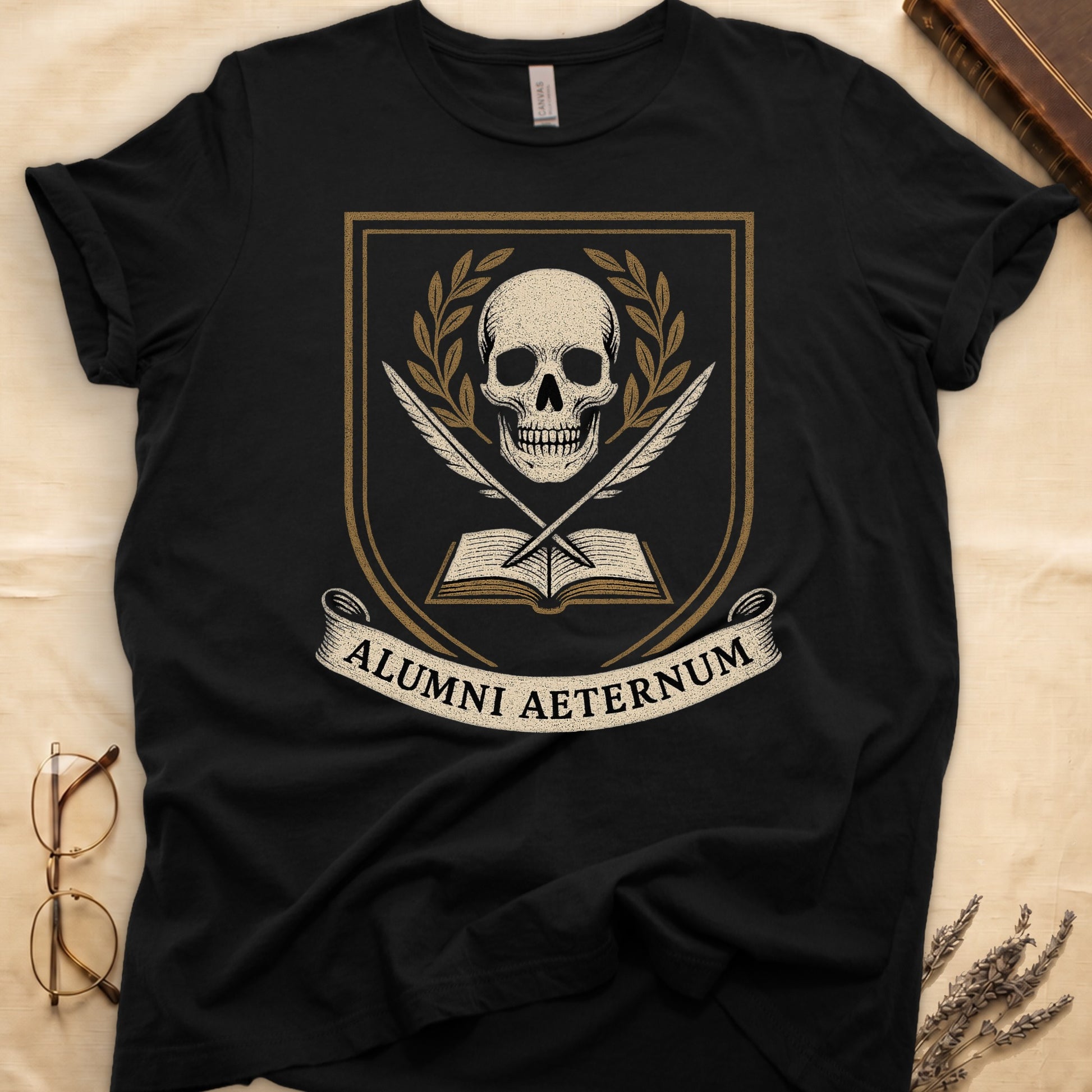Black tee with heraldic shield, skull and gold laurels, crossed quills, open book, scroll "ALUMNI AETERNUM" below.
