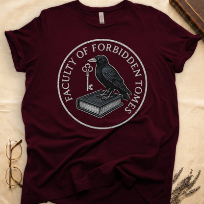 Navy tee with circular badge, raven on closed book holding key, "FACULTY OF FORBIDDEN TOMES" curved around in cream.