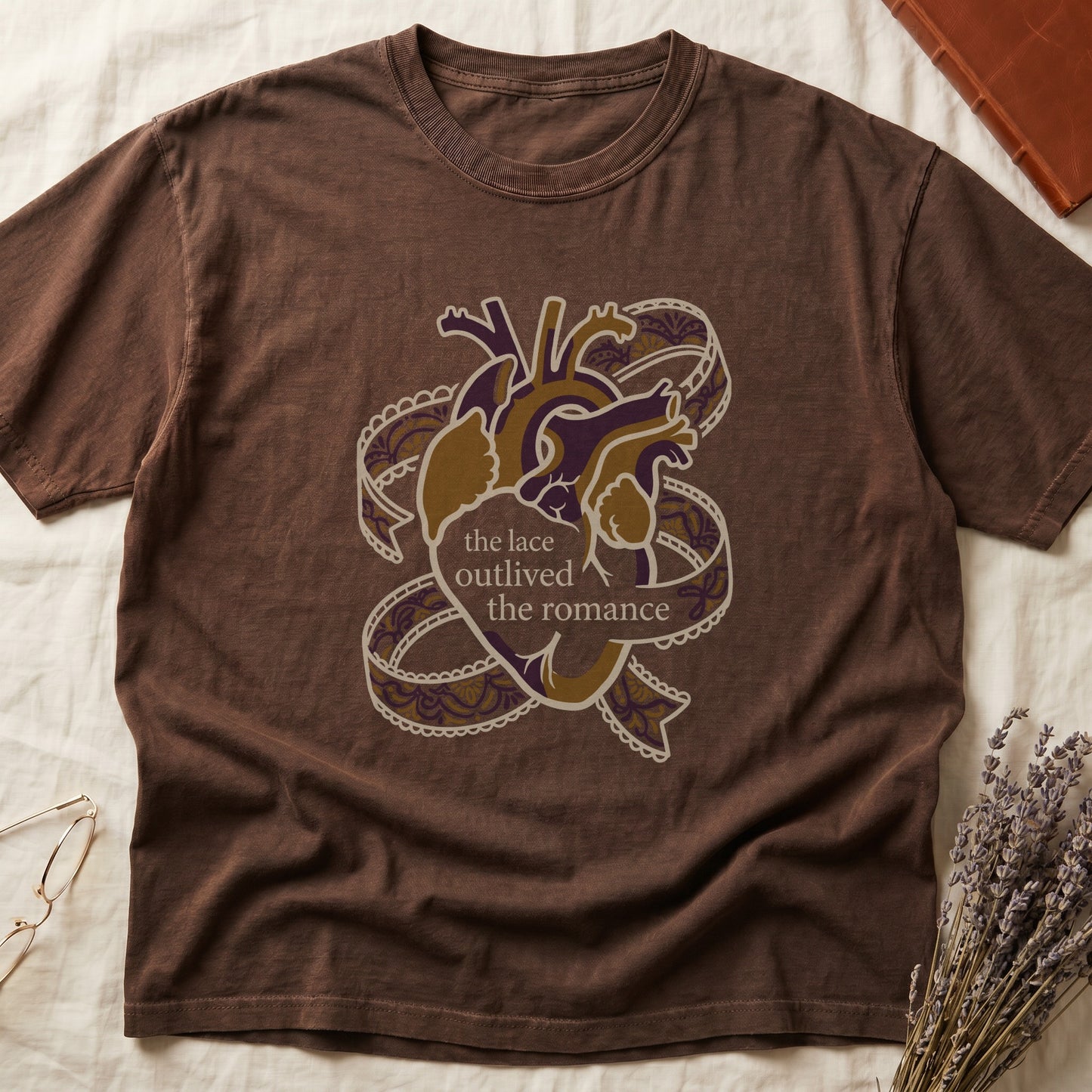 Espresso tee with anatomical heart in purple and gold wrapped in lace ribbons, "the lace outlived the romance" in serif.