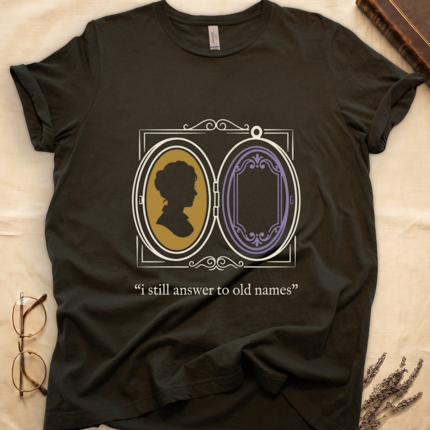 Military Green tee with Victorian double-locket, silhouette portrait in gold frame, "i still answer to old names" cream serif below.