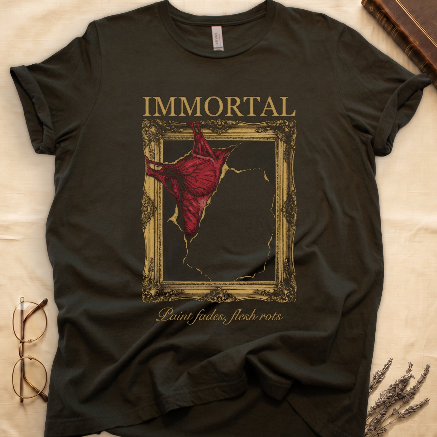 Military Green tee with gold frame and exposed muscle tearing canvas, "IMMORTAL" top, "Paint fades, flesh rots" italic below.
