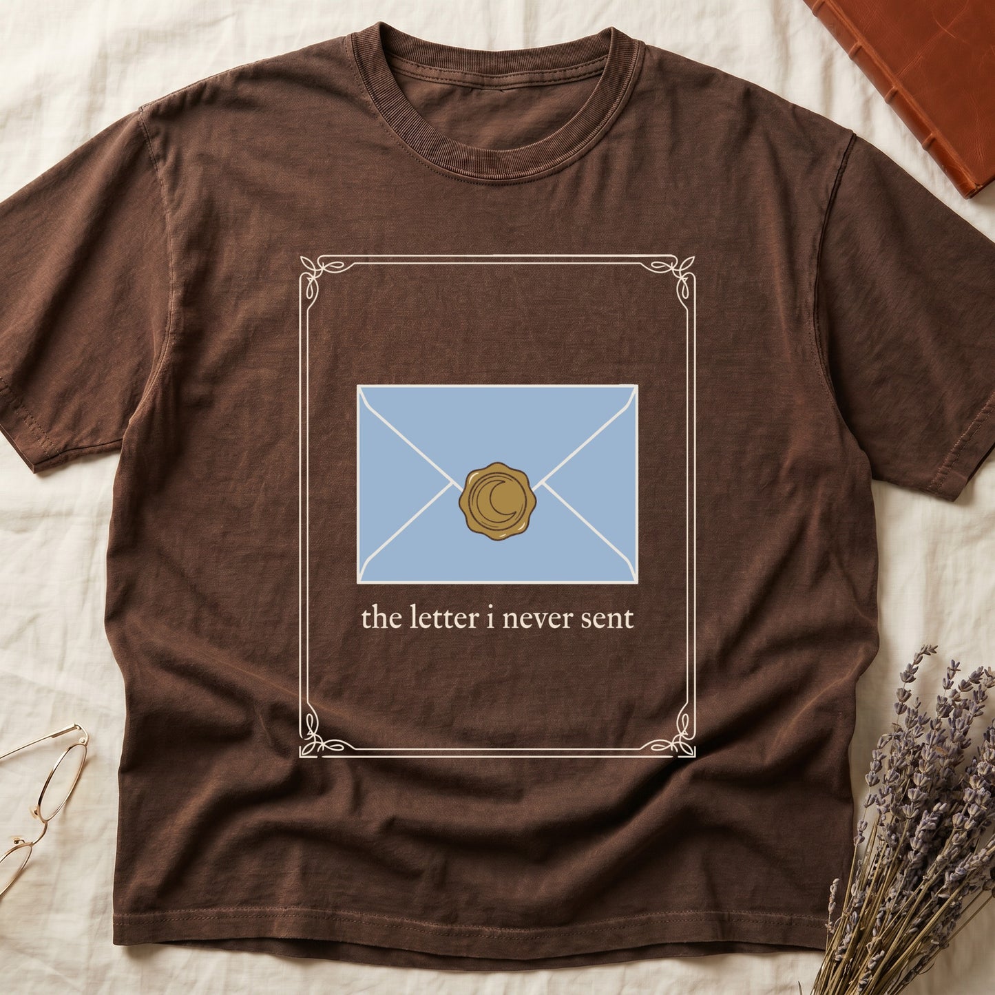 Espresso tee with pale blue envelope sealed with gold crescent moon wax seal, "the letter i never sent" cream serif below.