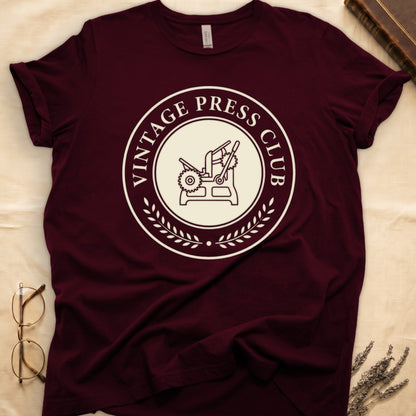 Maroon tee with circular letterpress badge, "VINTAGE PRESS CLUB" in serif capitals, antique printing press in cream linework.