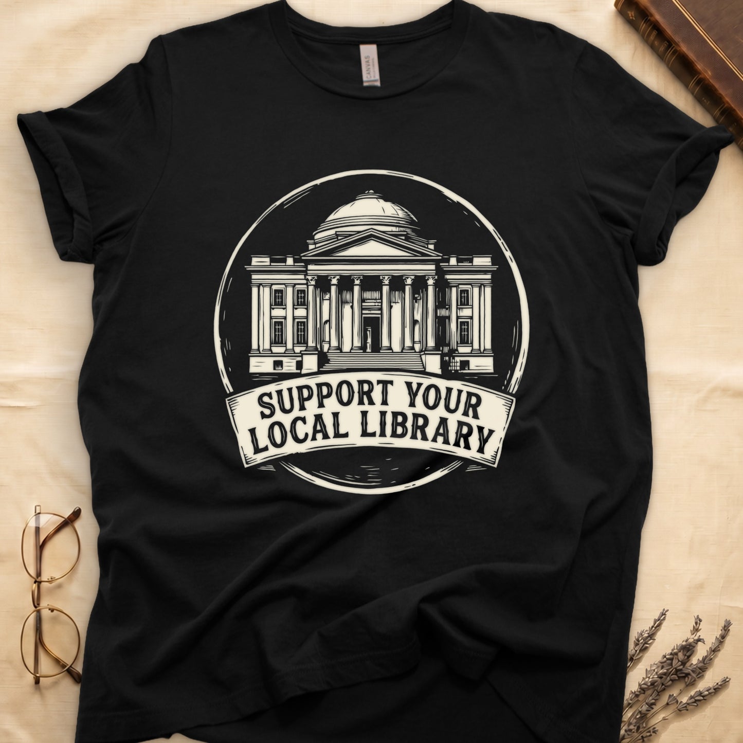 Black tee with circular cream badge of a classical library building, "SUPPORT YOUR LOCAL LIBRARY" on a banner below.