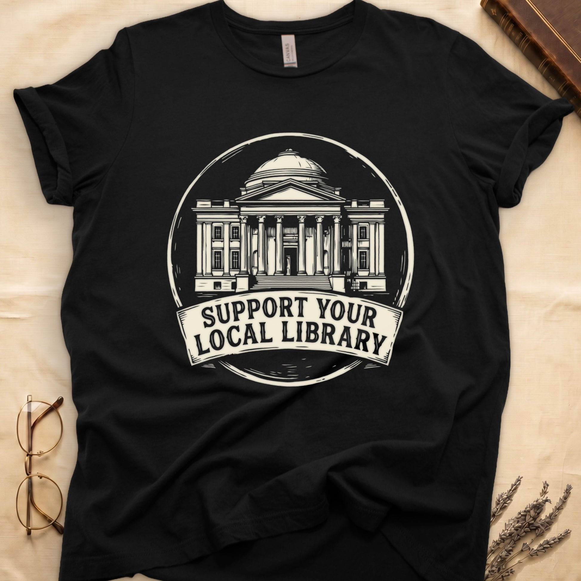 Black tee with circular cream badge of a classical library building, "SUPPORT YOUR LOCAL LIBRARY" on a banner below.
