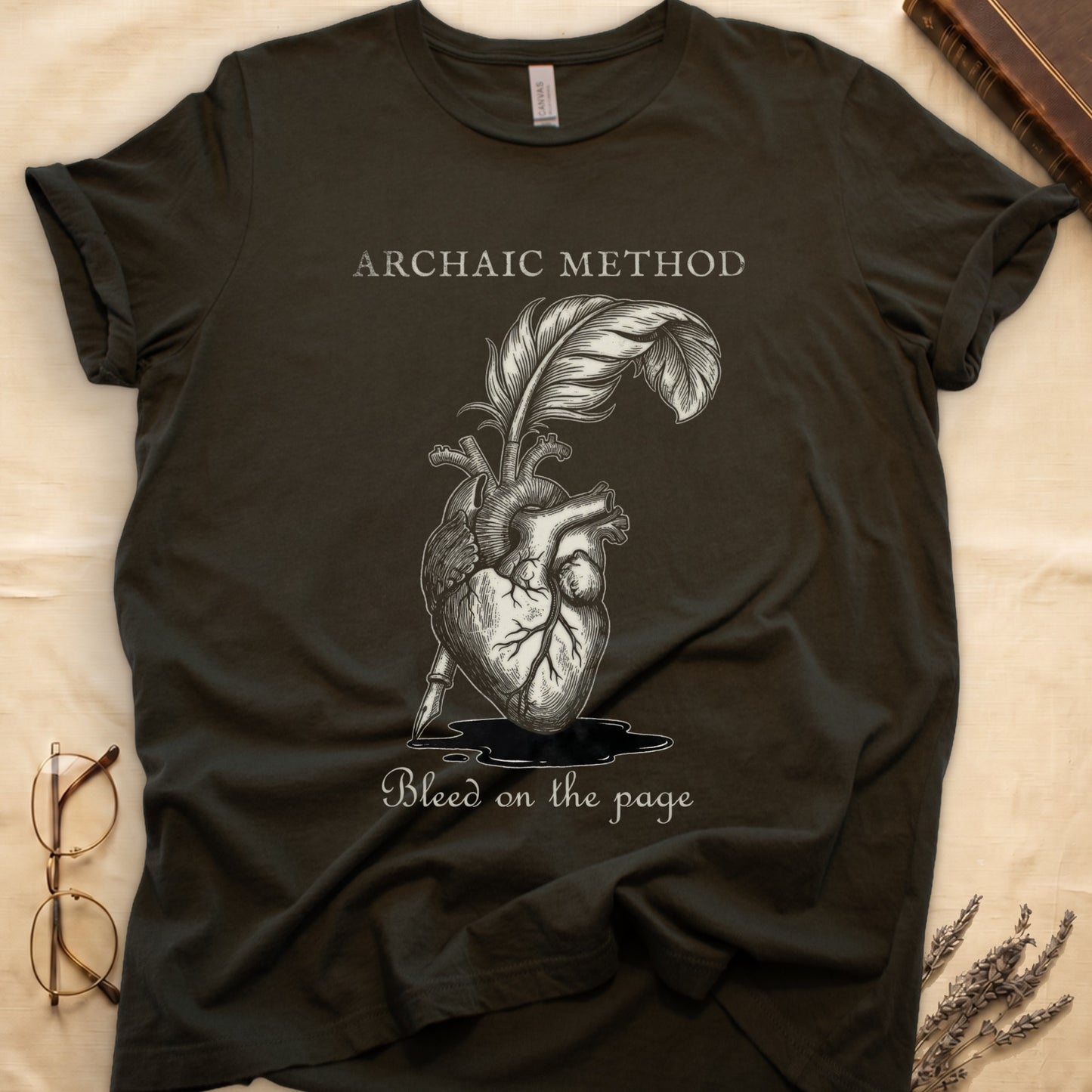 Military Green tee with anatomical heart and quill emerging in cream linework, "ARCHAIC METHOD" top, "Bleed on the page" below.