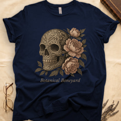 Navy tee with filigree-engraved skull on left, peach-cream peonies on right, crossed bones below, "Botanical Boneyard."