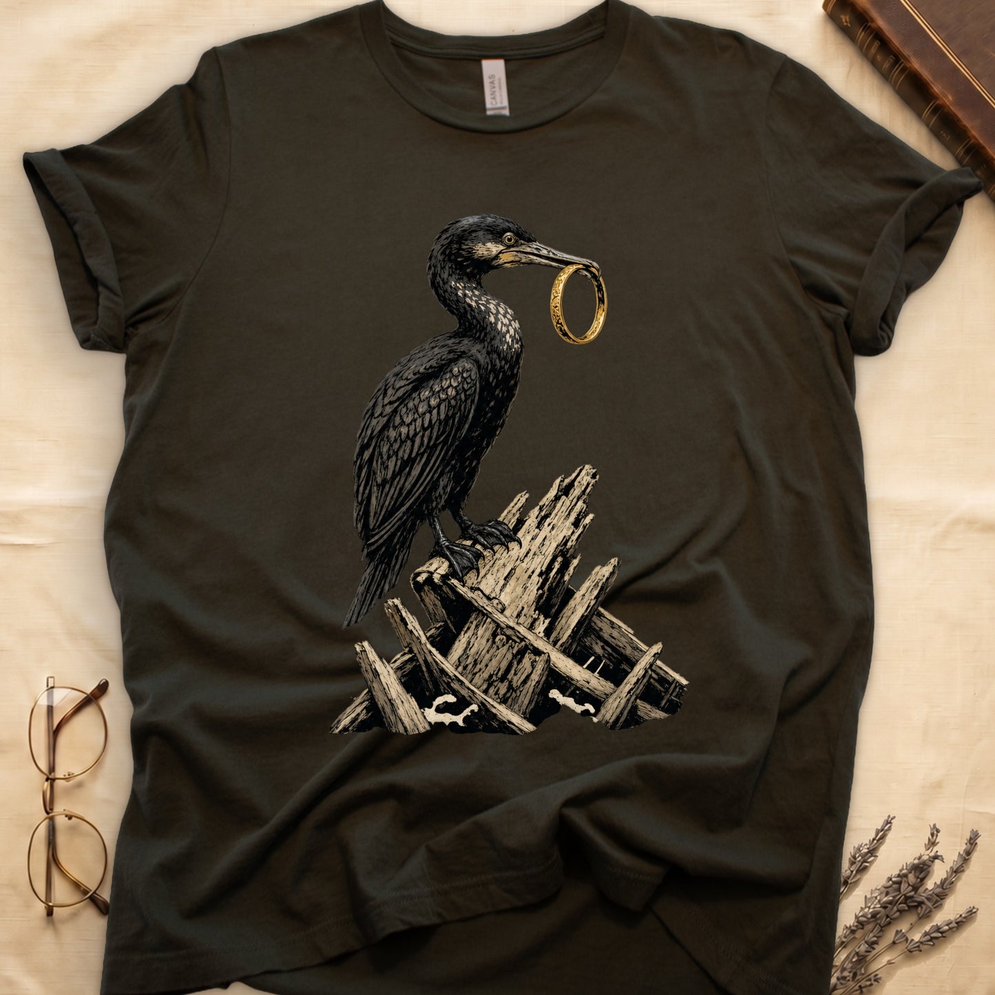 Dark t-shirt with a black bird holding a golden ring, perched on driftwood.