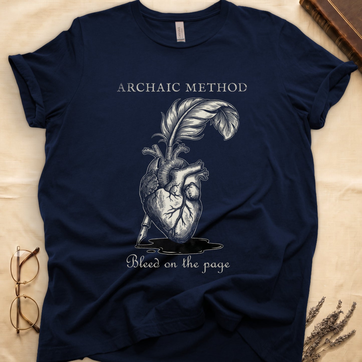 Navy tee with anatomical heart and quill emerging in cream linework, "ARCHAIC METHOD" top, "Bleed on the page" below.