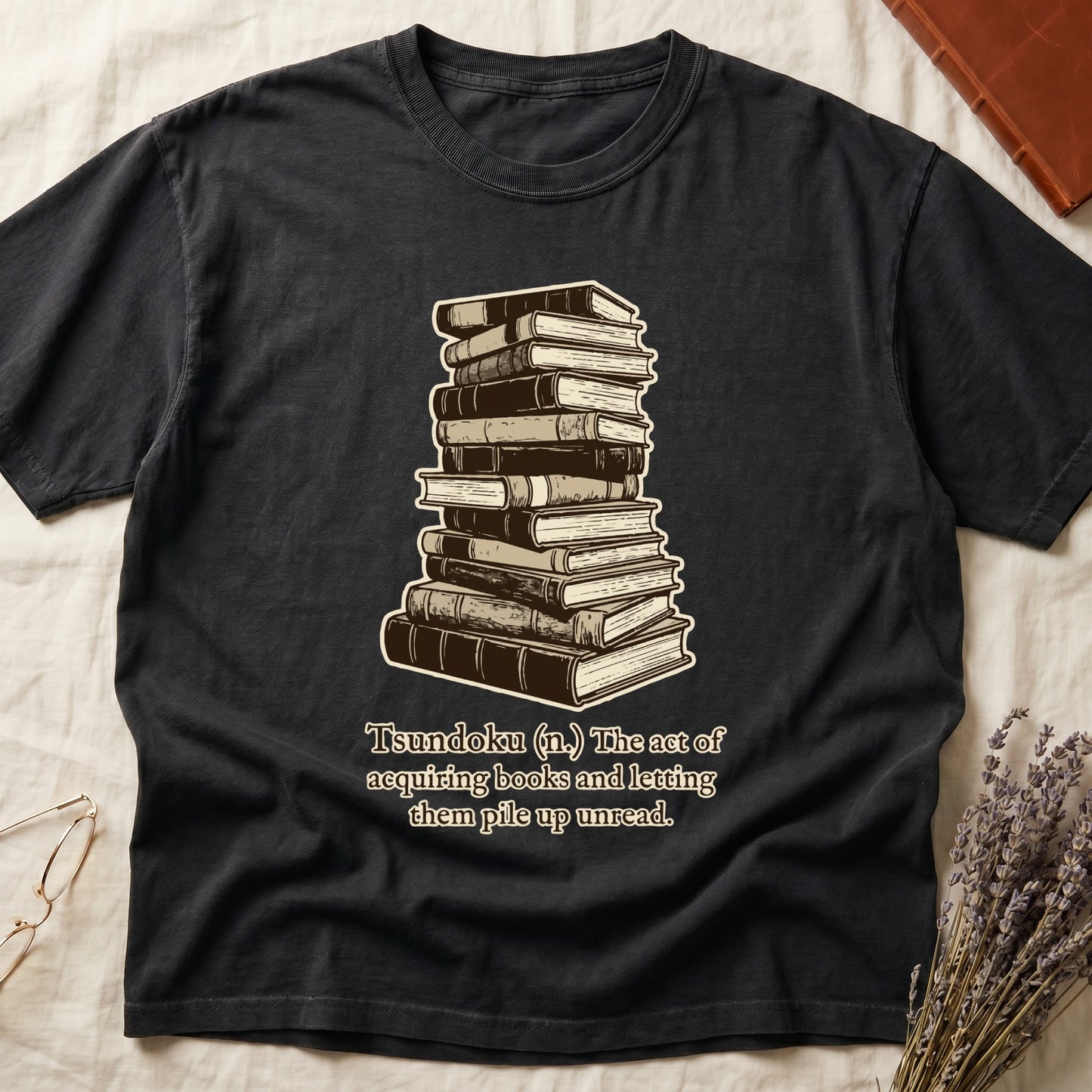 Black tee with stack of vintage hardcovers, "Tsundoku (n.) The act of acquiring books and letting them pile up unread."
