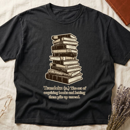Black tee with stack of vintage hardcovers, "Tsundoku (n.) The act of acquiring books and letting them pile up unread."