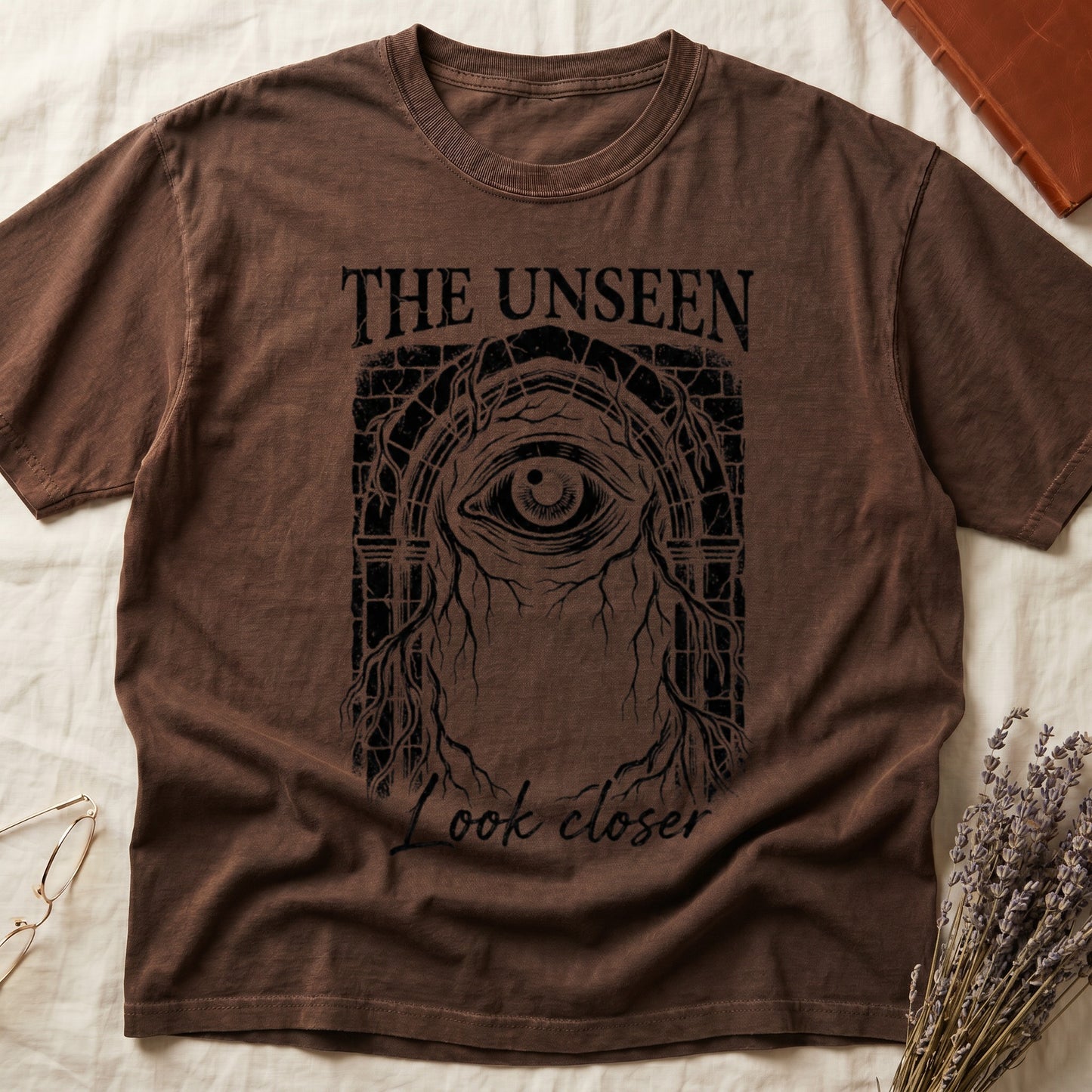 Espresso tee with Gothic stone arch, open eye, roots trailing, "THE UNSEEN" top, "Look closer" cursive below.