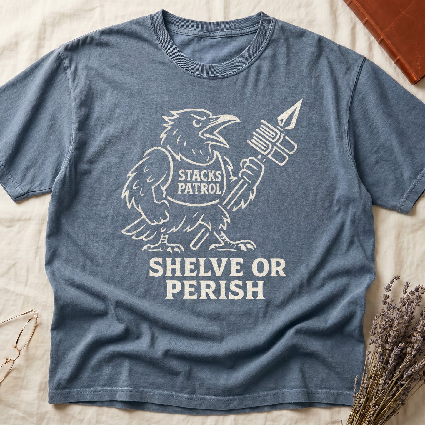 Blue Jean tee with vintage raven mascot, "STACKS PATROL" sash, feather pen aloft, "SHELVE OR PERISH" bold serif below.