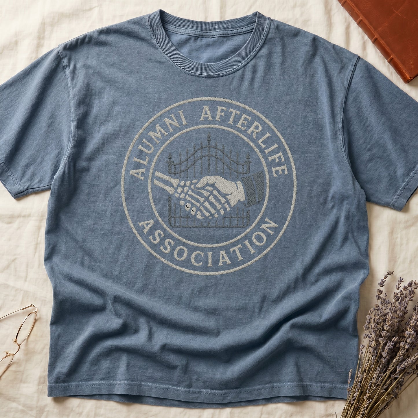 Espresso tee with embroidered patch, skeletal handshake at cemetery gate, "ALUMNI AFTERLIFE" top, "ASSOCIATION" bottom.