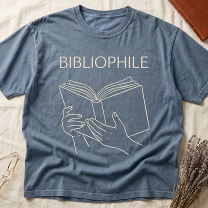 Blue Jean tee with two hands cradling an open book in cream and brown linework, "BIBLIOPHILE" in serif capitals above.