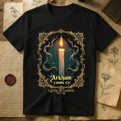 Black tee with lit candle, smoke, ornate gold filigree border, "Arkham Candle Co.," "Lighting the Darkness Since 1920."